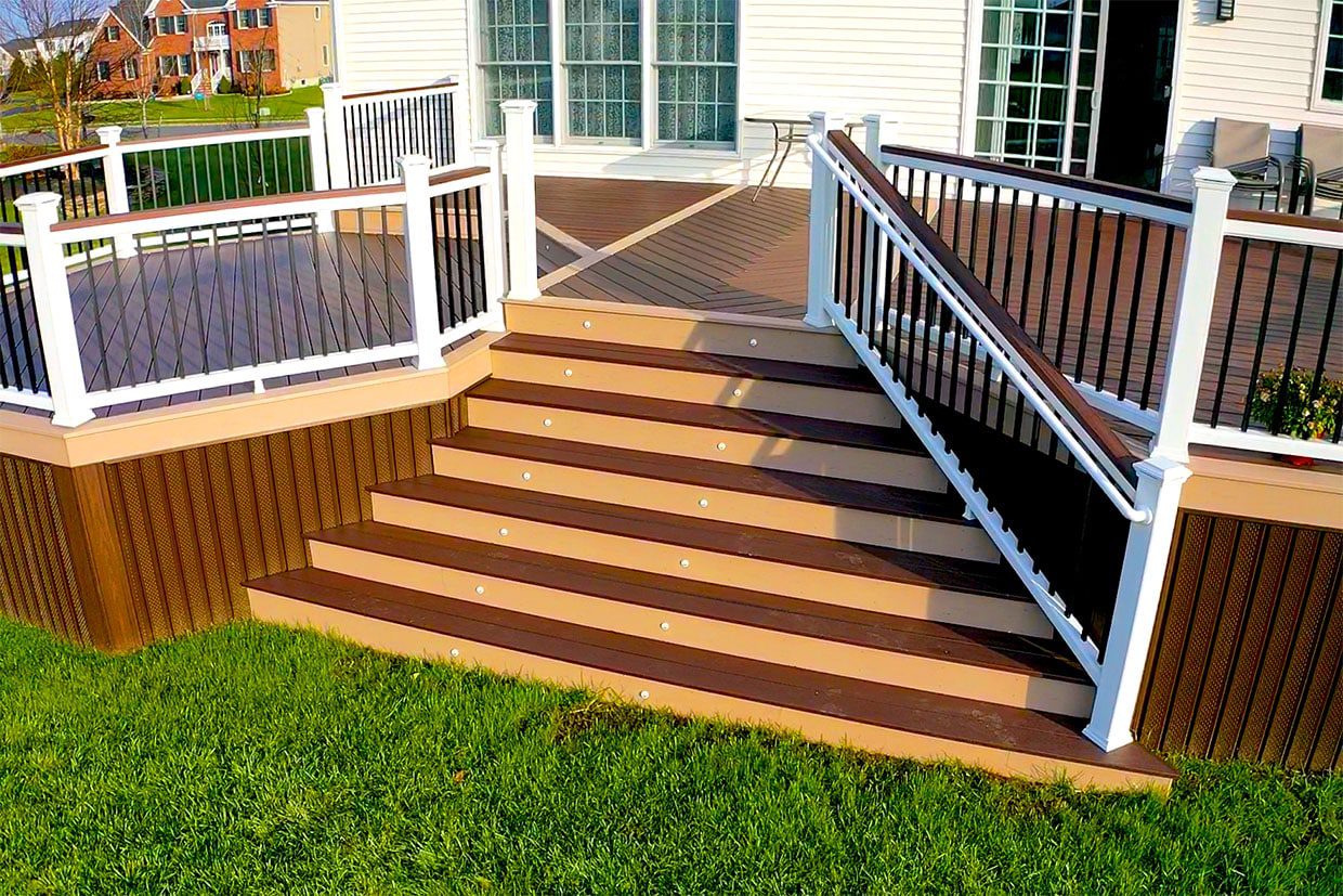 Wide, flared composite deck stairs with two-tone coloring and white railings leading to a grassy lawn.