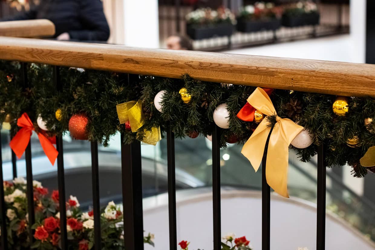 Deck railing decorated with Christmas garland, red and gold ornaments, and yellow bows.