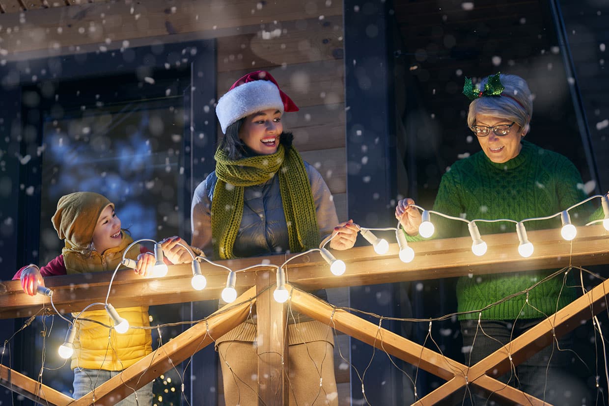 Family installing string Christmas lights for deck railing together on a snowy evening.