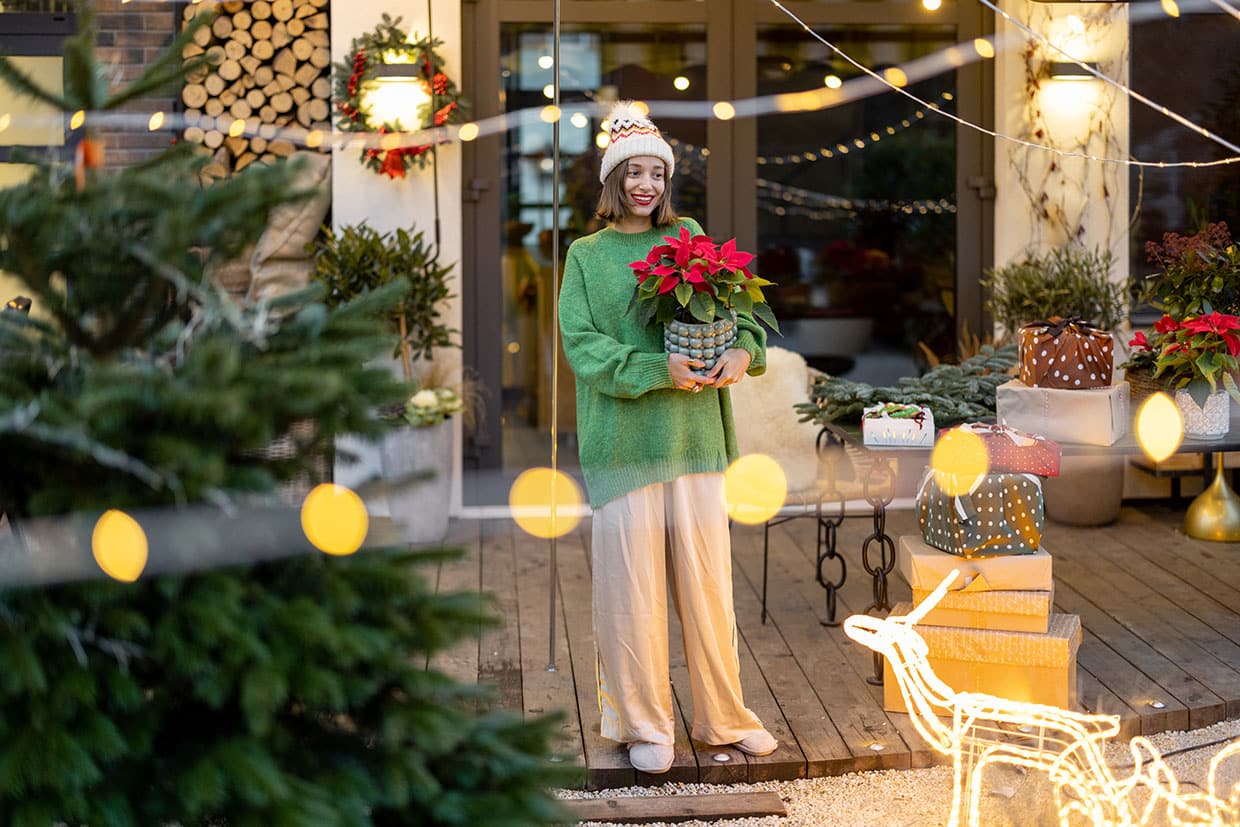 Woman holding red poinsettias for deck styling on a wooden patio adorned with Christmas lights for deck stringers, wrapped gifts, and a lighted reindeer figure.
