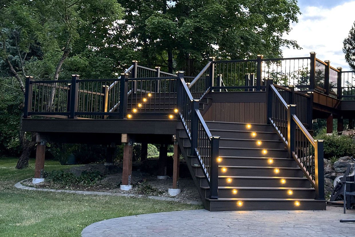 A multi-level composite deck featuring wide stairs with built-in riser lights and black metal railings.