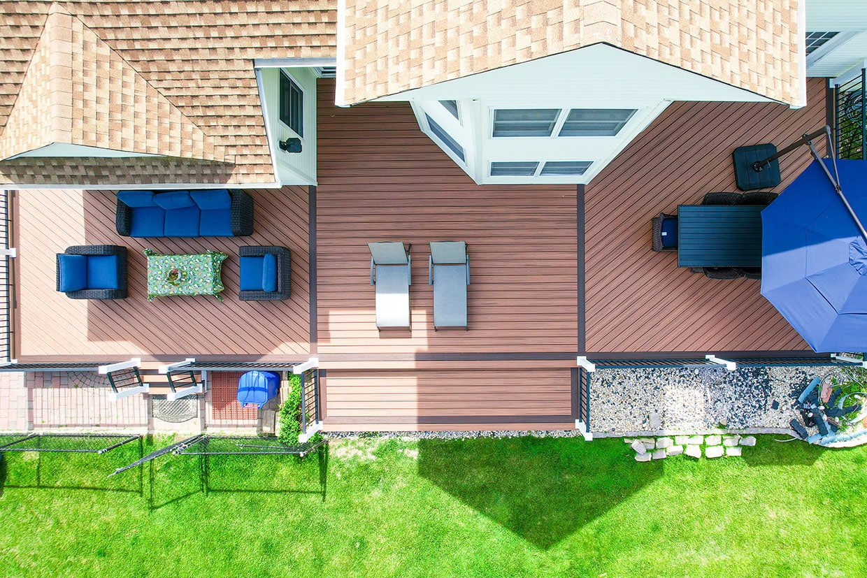 Aerial view of a spacious multi-level backyard deck featuring dining and lounge areas, visually demonstrating how an expanded living space answers the question 'does a deck add value to a home'.