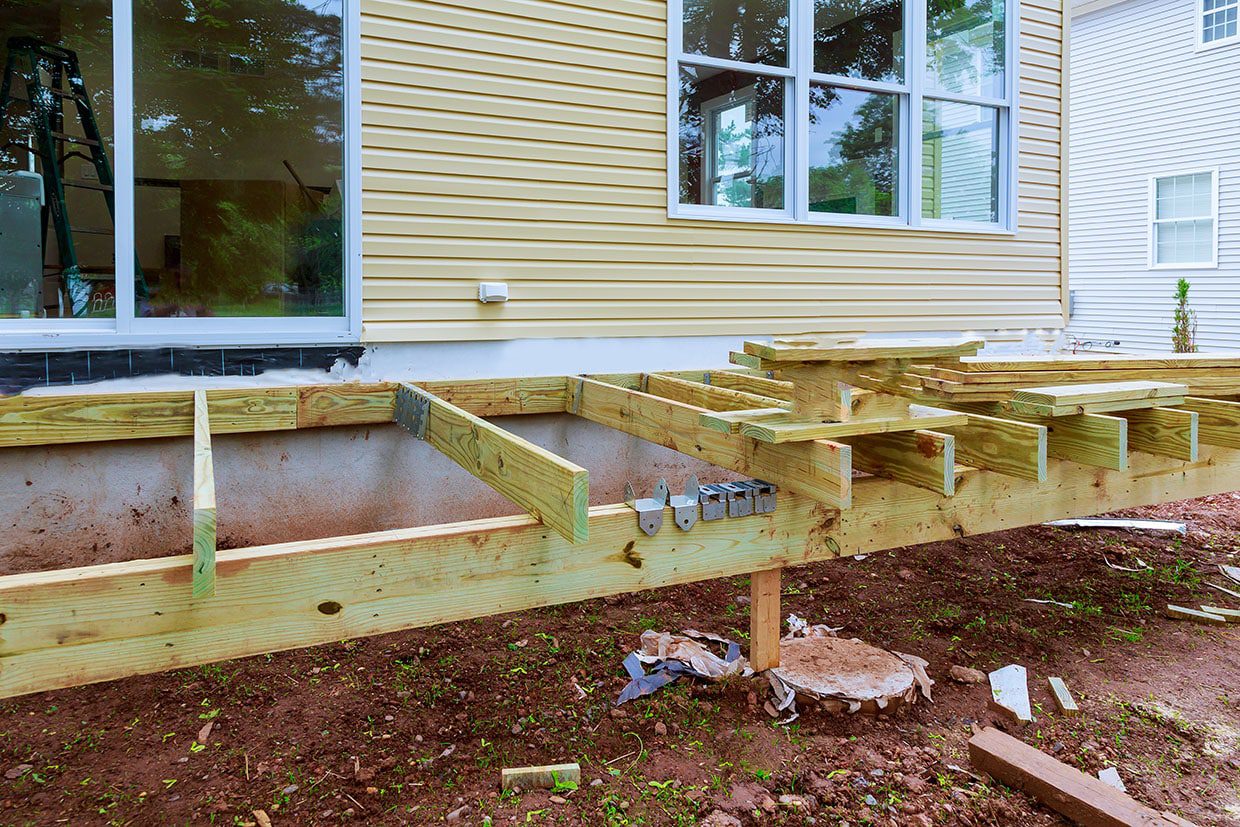 A partially constructed deck frame attached to a house, displaying ledger board installation and installed joist hangers.
