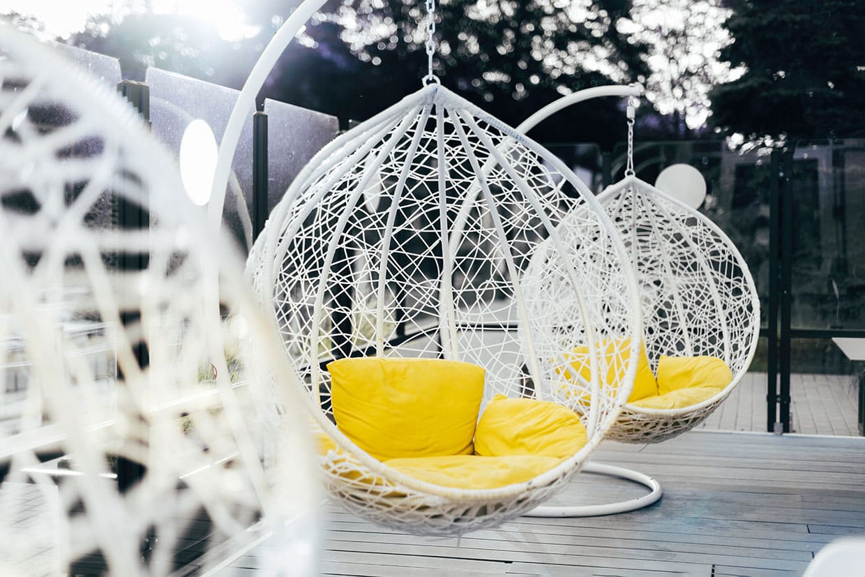 Two white hanging egg chairs with bright yellow outdoor cushions on a wooden deck.