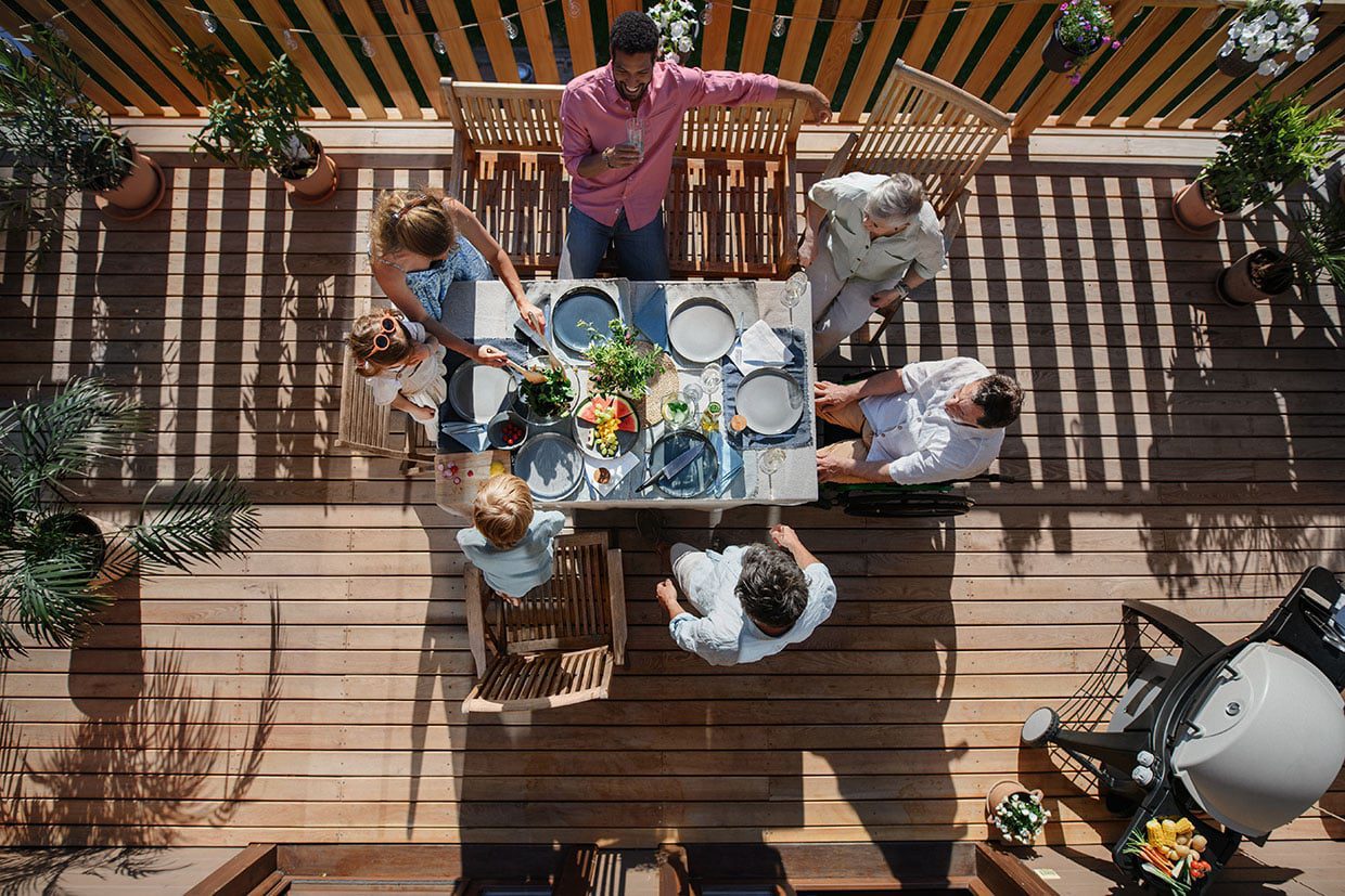 Overhead view of a multi-generational family enjoying a meal together at a dining table on a sunny wooden deck.