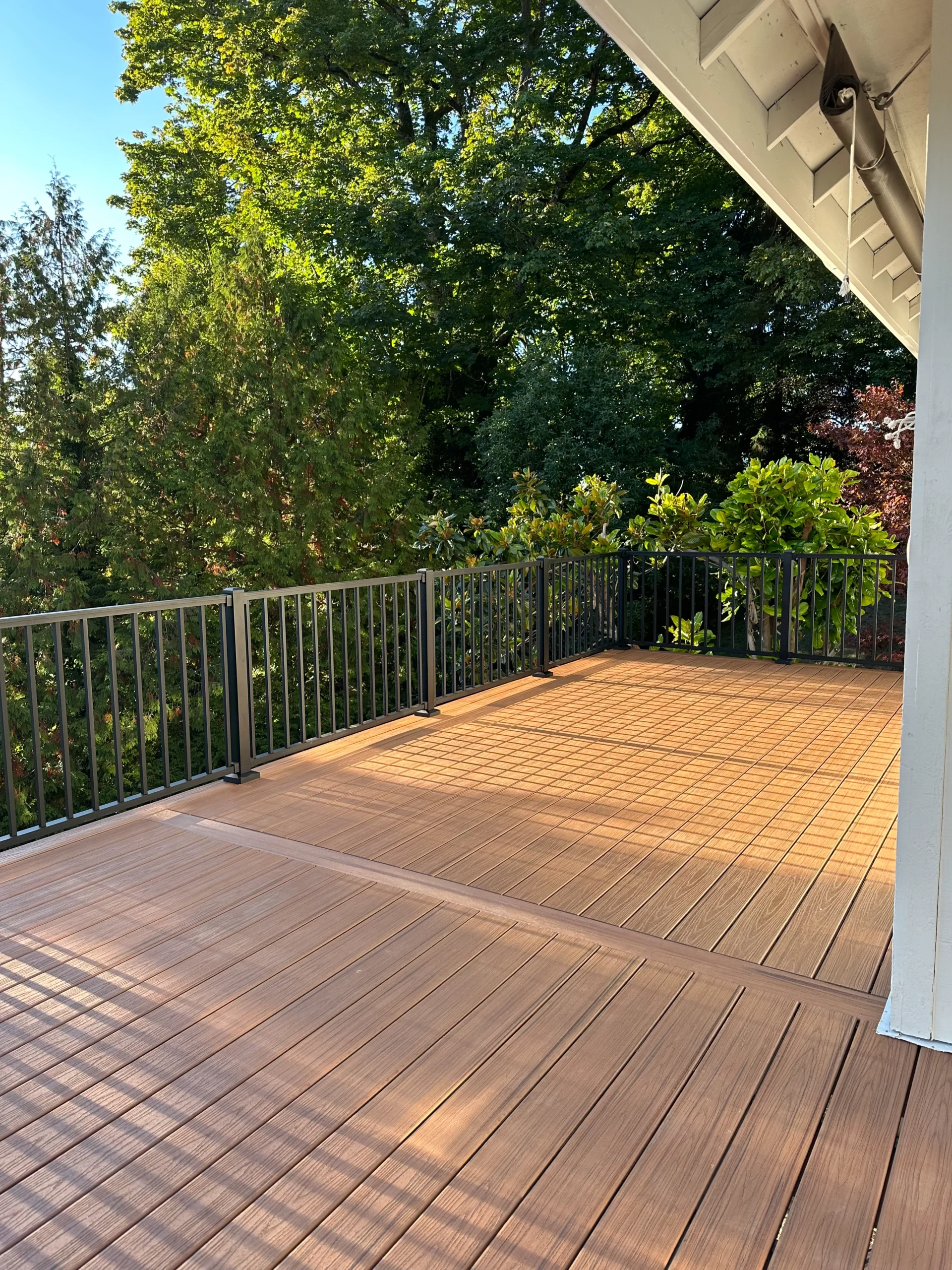 A sunlit outdoor space featuring warm brown composite decking and sleek black metal railings, showcasing versatile decking designs and ideas for Seattle homes.
