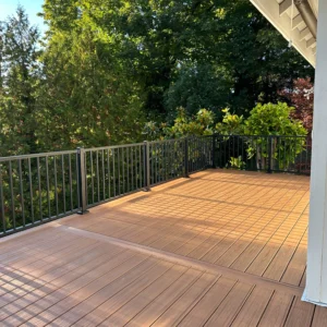 Outdoor decking design with warm wood tones, surrounded by lush greenery and a modern railing, showcasing decking designs and ideas.