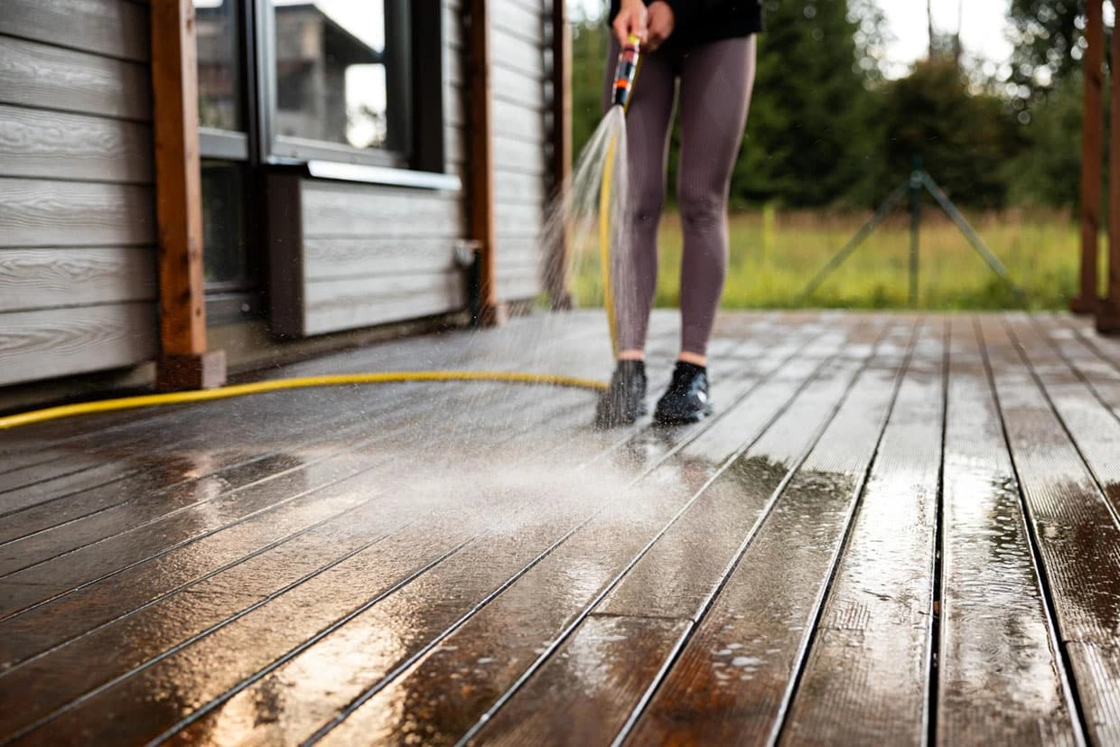A person cleaning a composite deck using a water hose, learning how do I build a deck