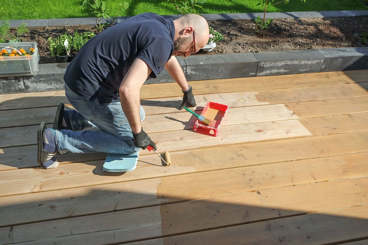 A worker applies a finish to new deck boards as part of a deck resurfacing Seattle project.