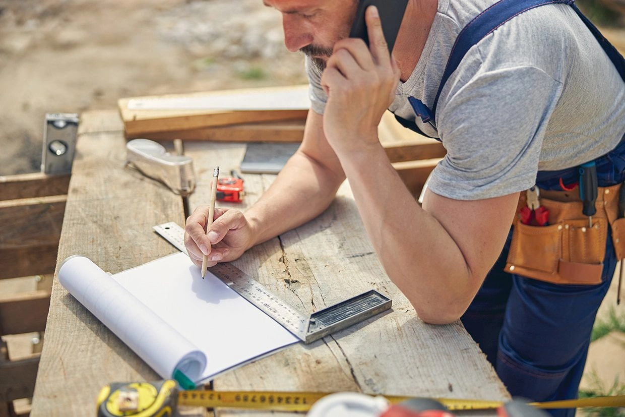 A worker is on the phone and taking notes while planning a deck resurfacing project in Seattle.