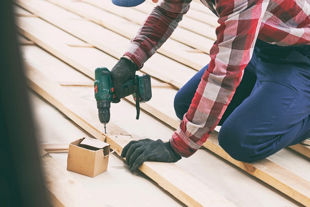A person using a cordless drill to secure wooden planks, learning how do I build a deck