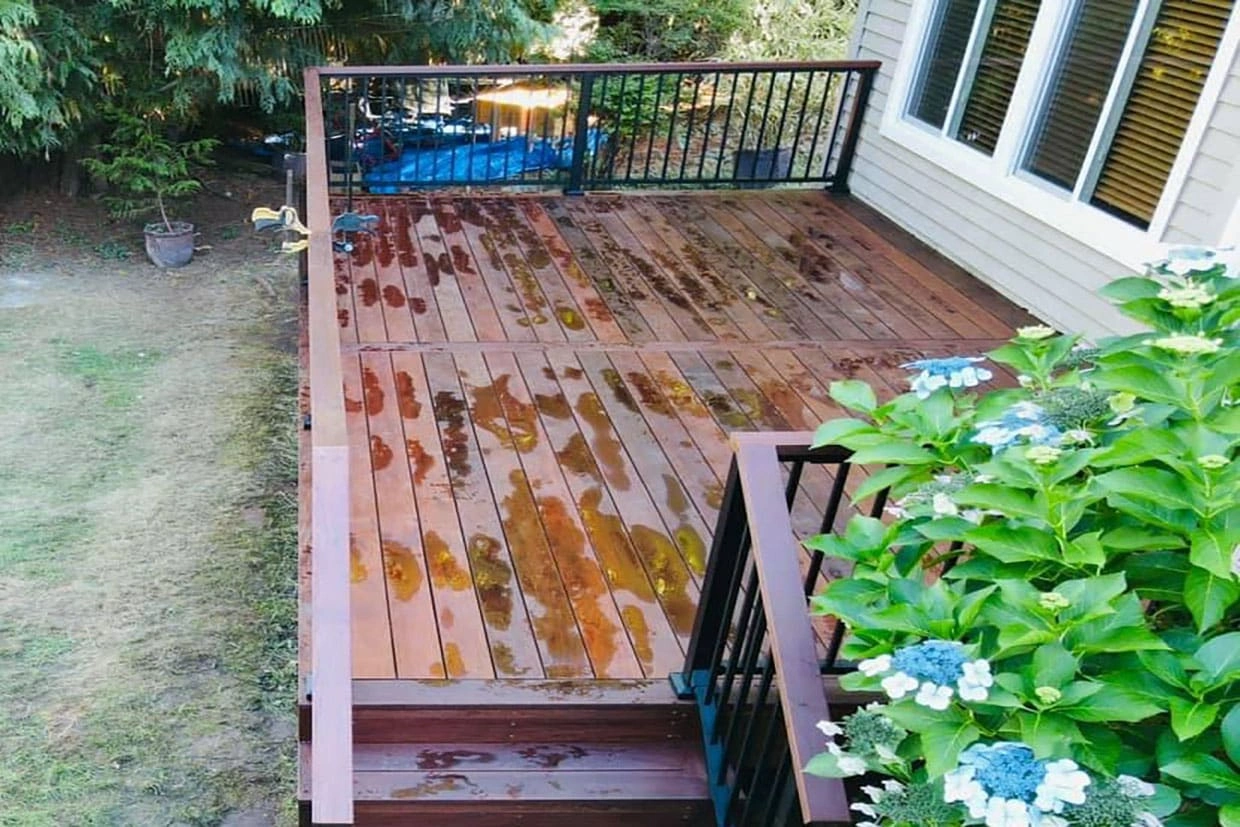 A deck with a wooden finish, partially wet, featuring black railings, showcasing a durable Composite Deck Installation.