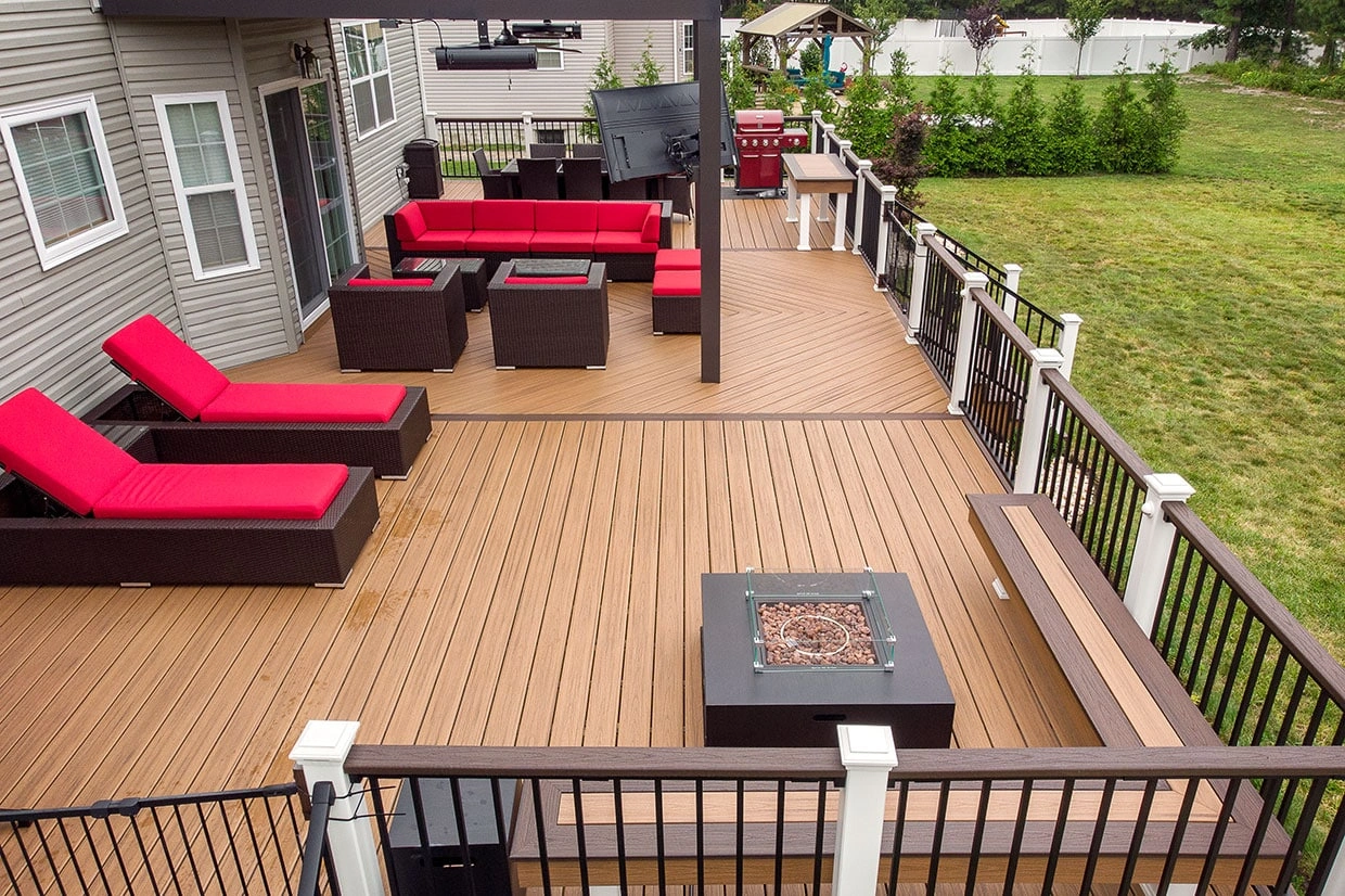 A spacious deck featuring red outdoor seating, a firepit, and sleek railings, highlighting deck installation trends