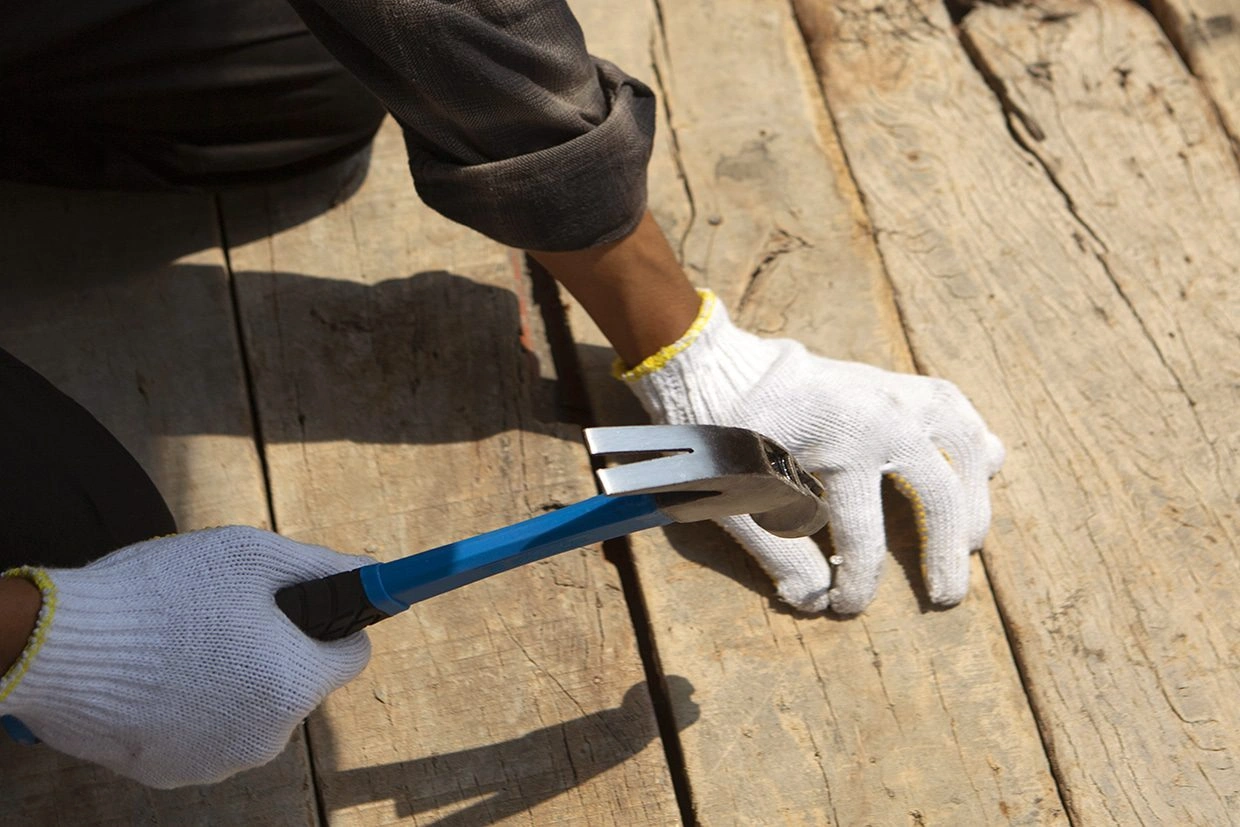A worker using a crowbar to remove old deck planks, preparing to Replace Deck Railings for enhanced safety.