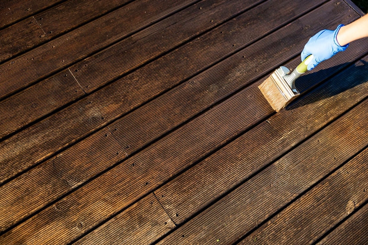 A person staining a wooden deck to enhance its durability, a key aspect of Deck Resurfacing vs Replacement Washington