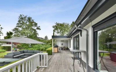Spacious outdoor deck with comfortable furniture, a shade umbrella, and green garden surroundings.