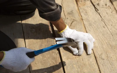 Seattle deck resurfacing shown as gloved hands use a hammer to remove a raised nail from weathered wooden deck boards.