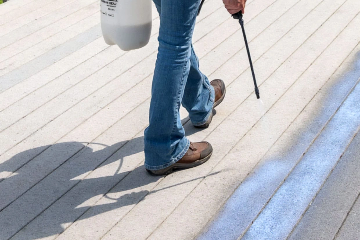 Seattle deck resurfacing with a worker spraying waterproofing sealant across light deck boards using a pump sprayer.