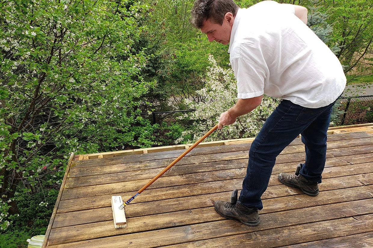 deck restore A person brushing a wooden deck as part of deck maintenance before restoration.