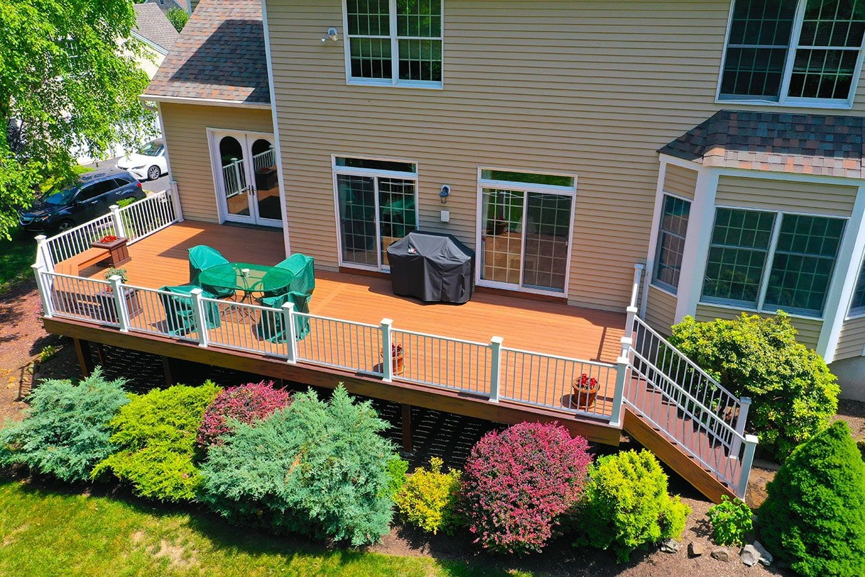 An elevated pet deck with warm brown decking, white railing, and stairs, centered around a grill and green seating.