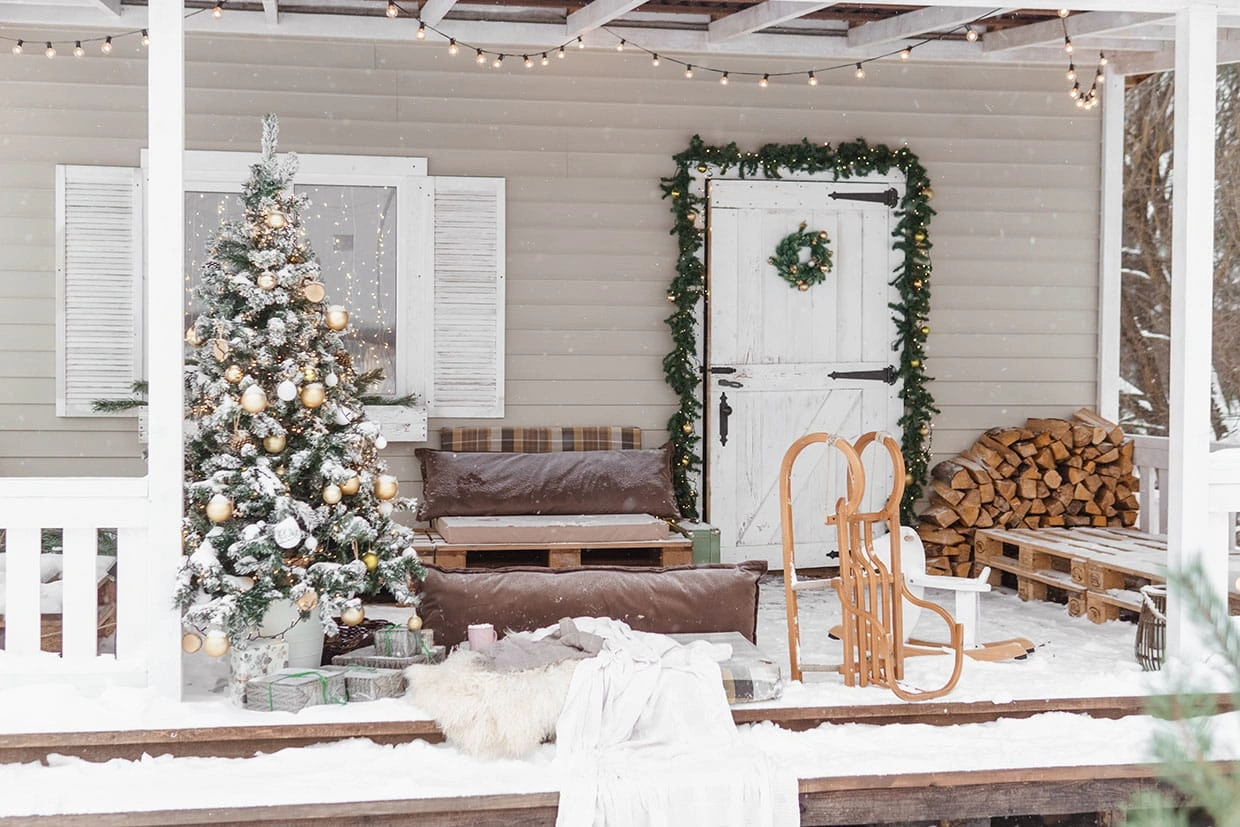 A covered porch festively decorated for Christmas with a tree, string lights, and pallet furniture, showing how a durable deck surface withstands winter snow and moisture exposure.