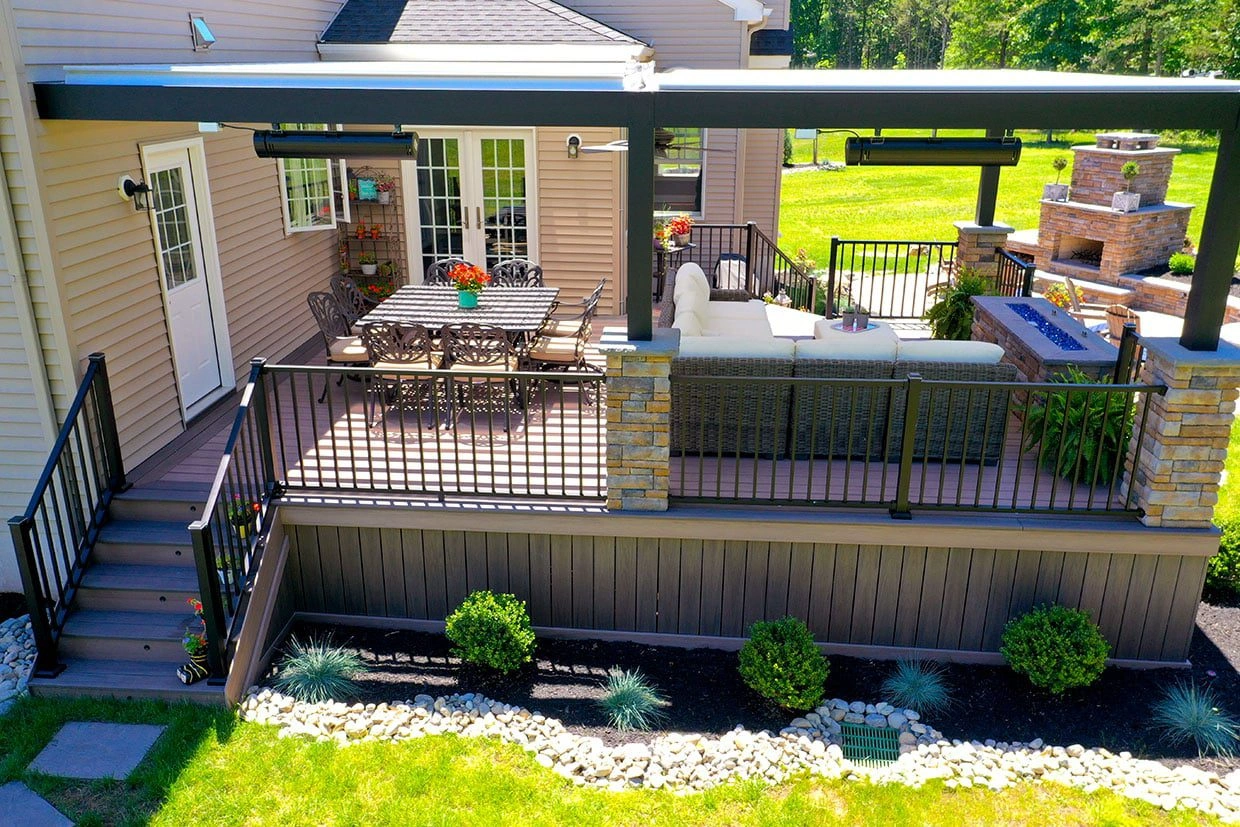 Luxury covered composite deck and patio featuring stone pillars, integrated heating, and a stone fireplace, showcasing expert work from a Bellevue patio contractor.
