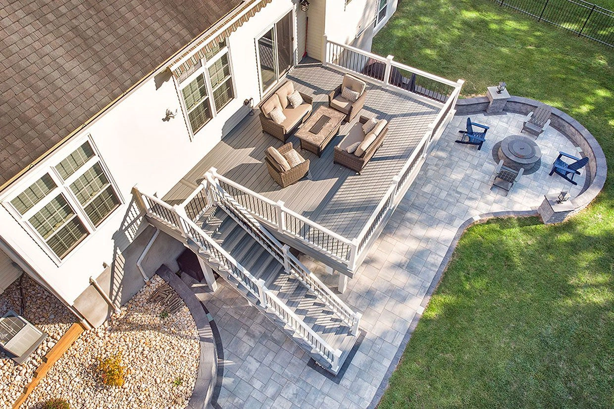 Aerial view of a multilevel backyard featuring a composite deck, stone patio, and circular fire pit area where to find reliable reviews about deck companies.