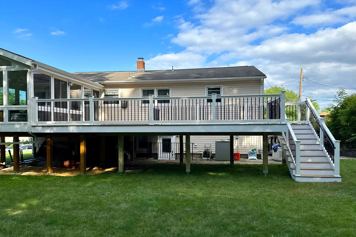 Rear exterior view of a suburban house featuring an elevated deck with composite railing and stairs, next to a sunroom where to find reliable reviews about deck companies.