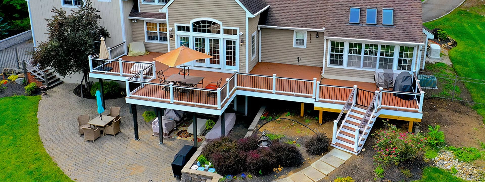 Large elevated deck with white railings and dual staircases leading to a brick patio, highlighting expert construction by a Bellevue patio contractor.
