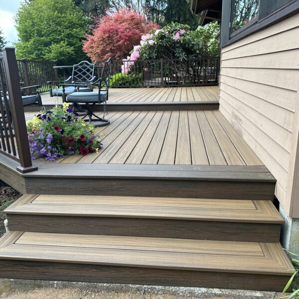 A wide view of multi-level composite deck stairs featuring wood-grain finish boards, dark brown railings, and integrated garden planters, showing proper flow and safety.