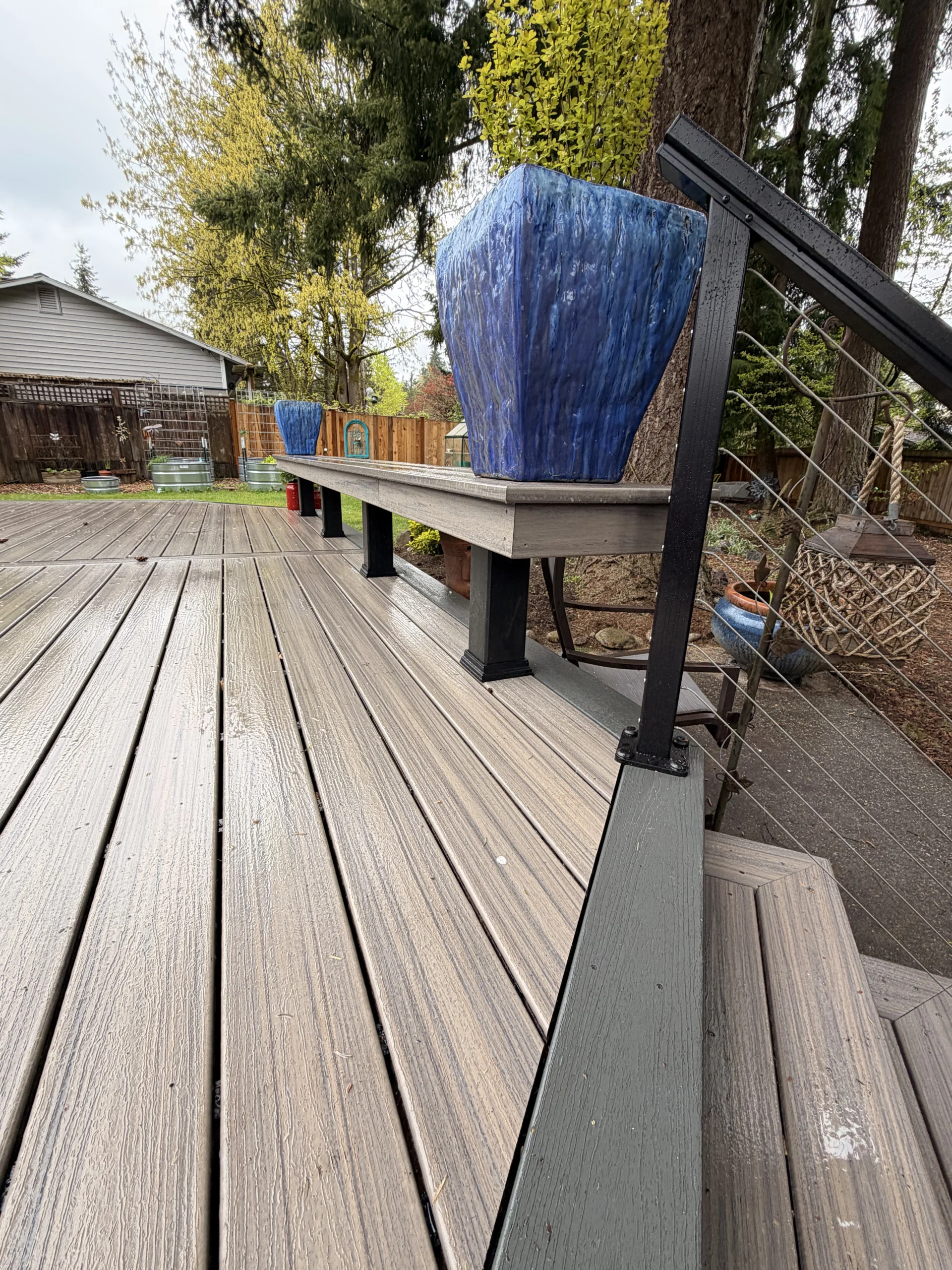 Wet grey boards next to a matching built-in bench with blue planters from a Composite Deck Installation in Seattle WA.