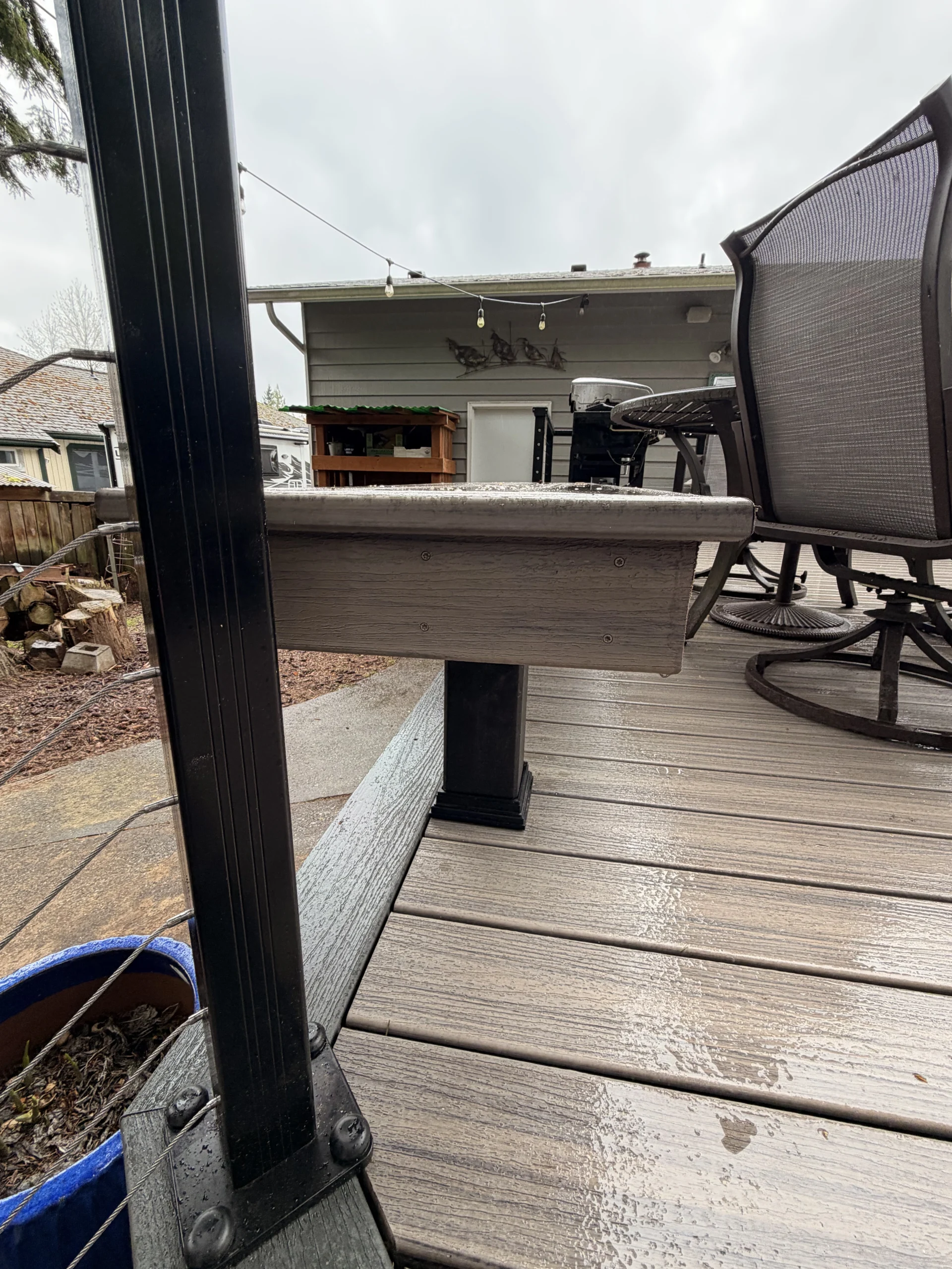 Profile view of a custom grey bench on a Composite Deck Installation in Seattle WA next to patio chairs.