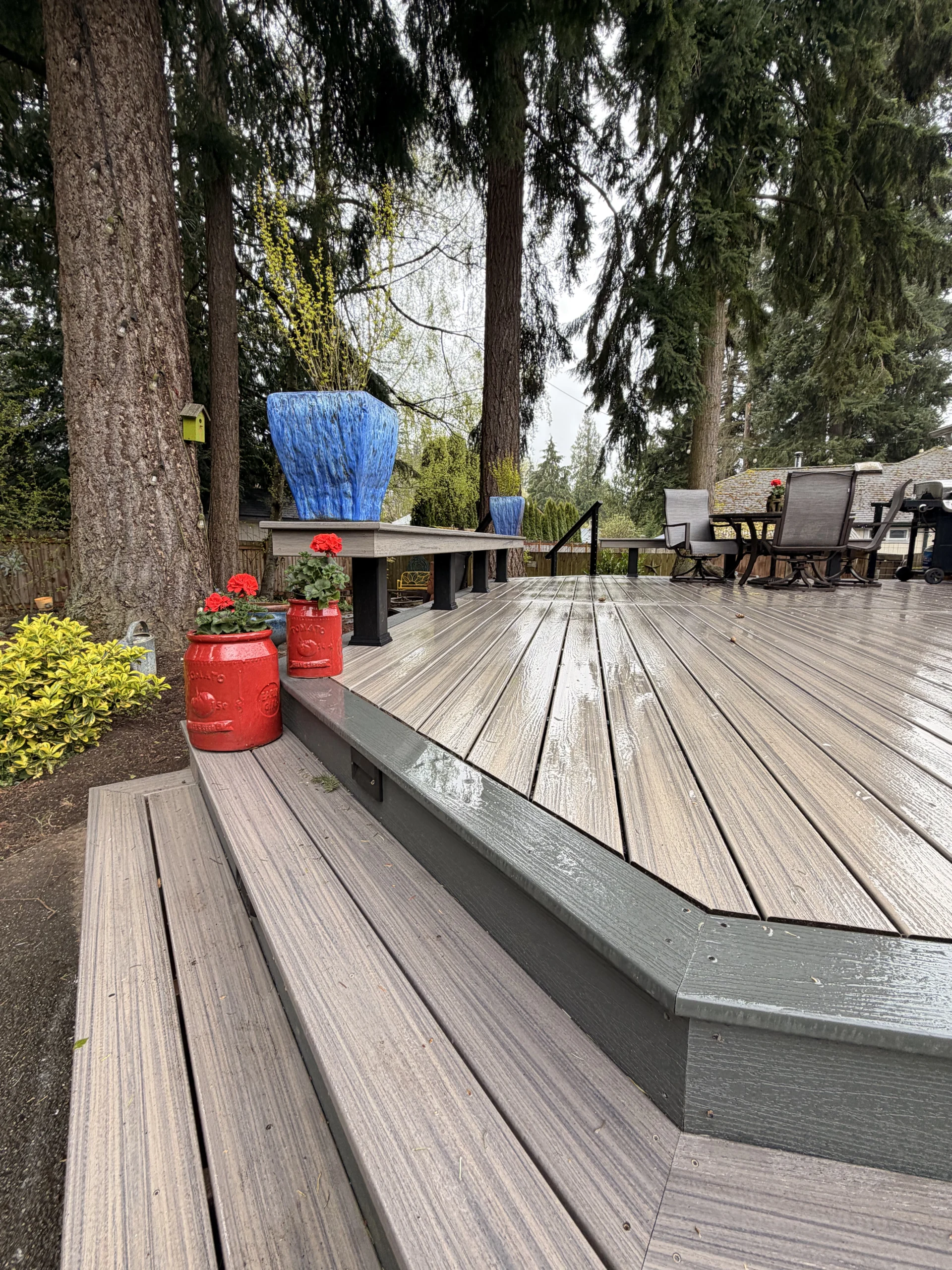 Red and blue planters decorate a finished Composite Deck Installation in Seattle WA surrounded by tall trees.
