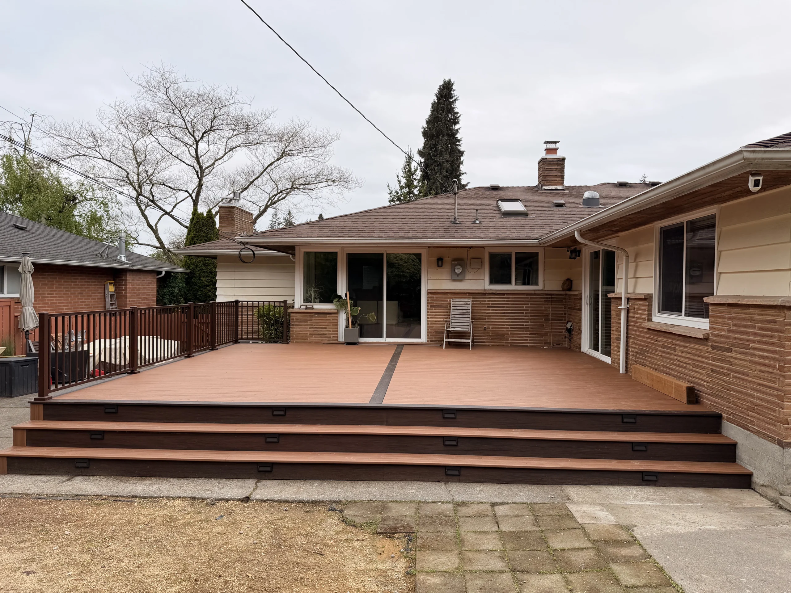 Full View of Custom Composite Deck Installation in Issaquah WA A wide composite Deck Installation in Issaquah WA with long steps and brown railings against a house.