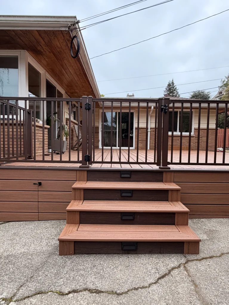 A vertical view of a composite deck installation in Issaquah WA with safety gates and lighted steps on a concrete patio.