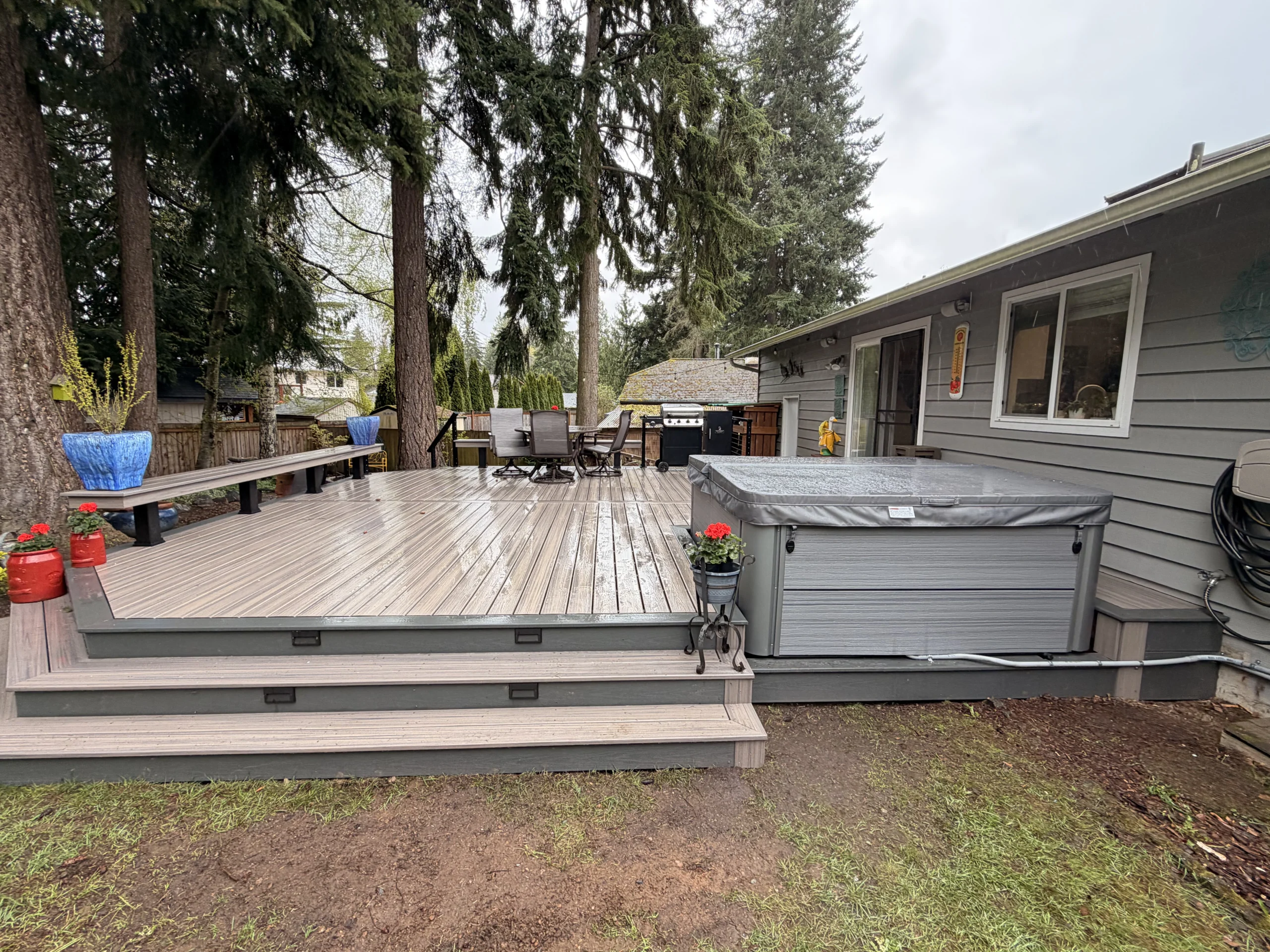 Modern Composite Deck Installation in Seattle WA featuring a built-in hot tub, wide steps, and surrounding pine trees.