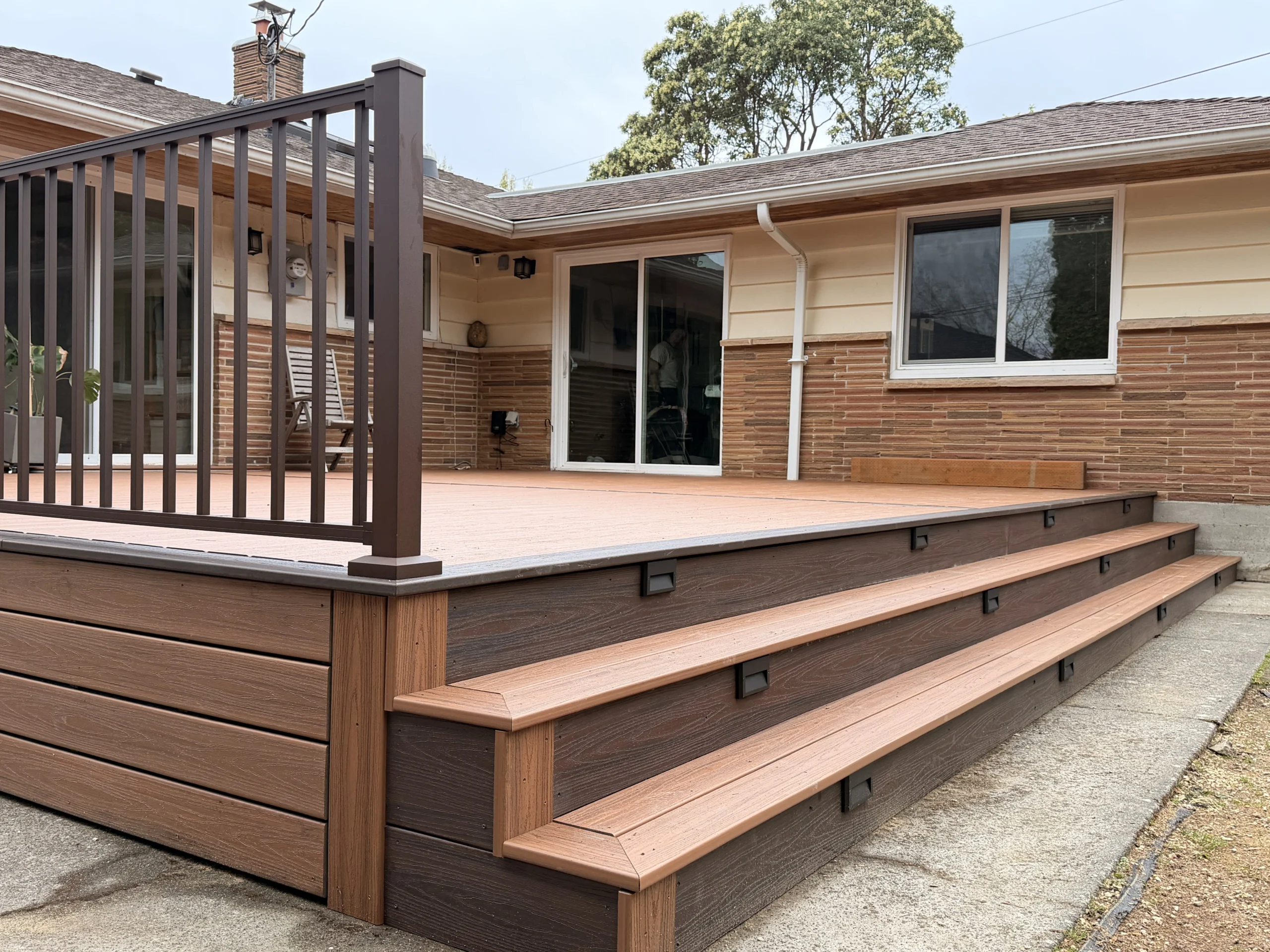 Modern Composite Deck Installation in Issaquah WA A new composite deck installation in Issaquah WA featuring multi-level steps, dark brown railings, and integrated riser lights.