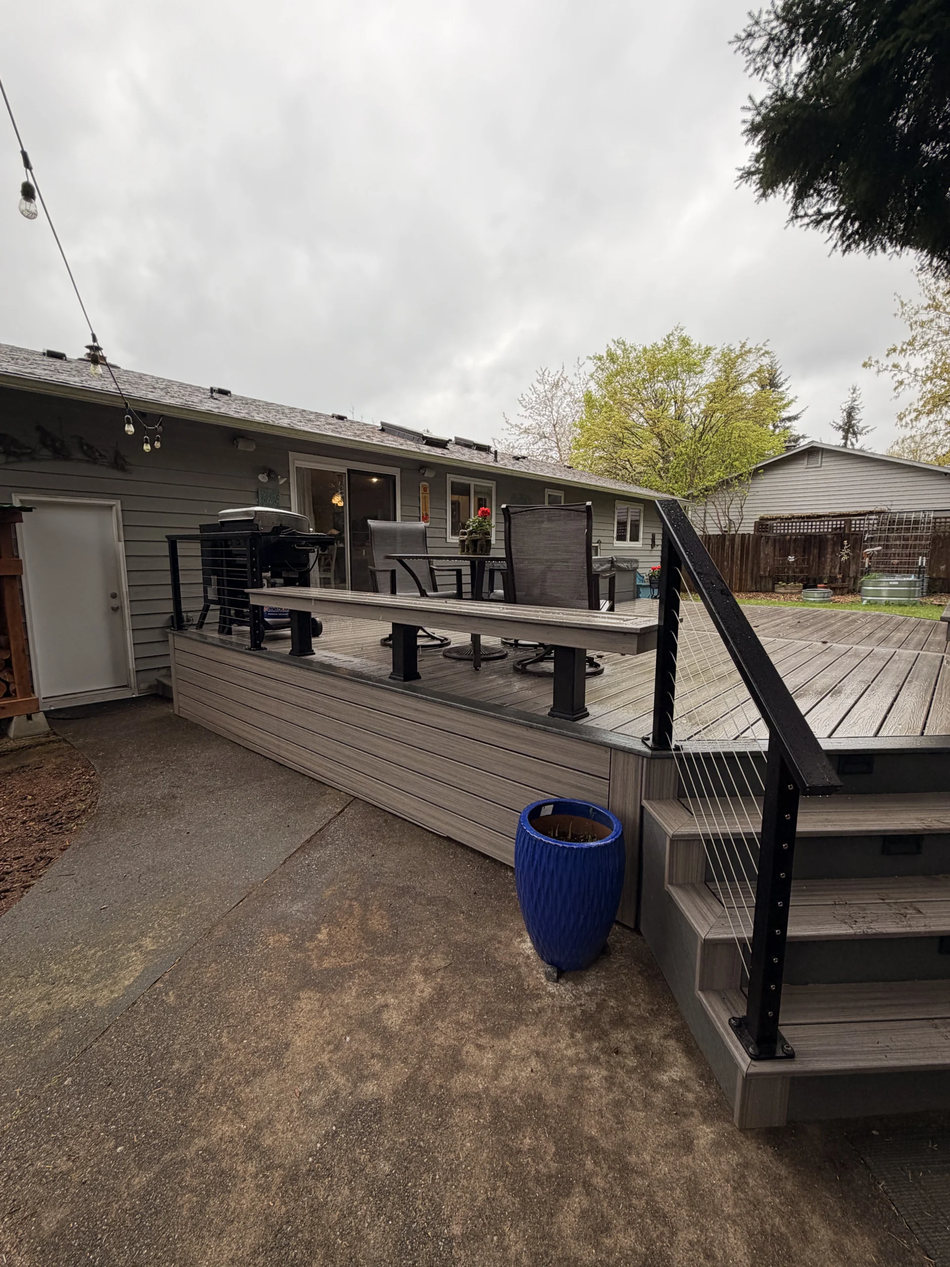 Completed Composite Deck Installation in Seattle WA featuring grey boards, modern black cable railings, and patio furniture.