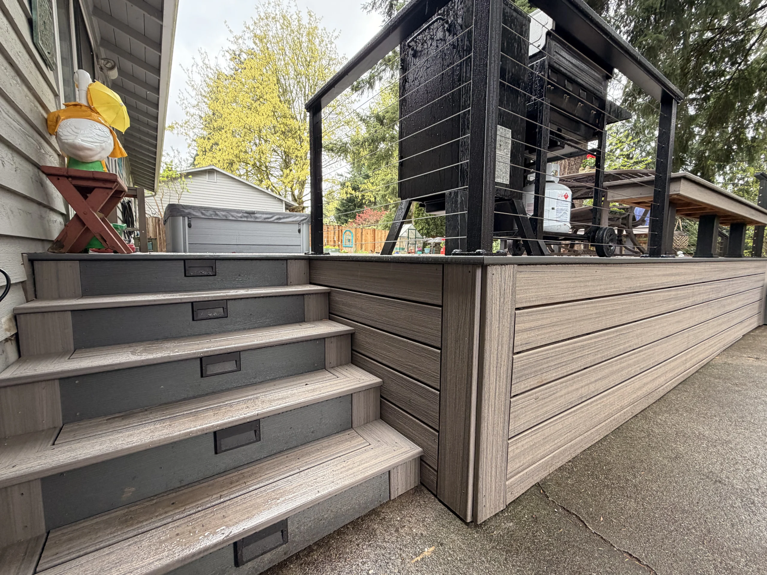Side view of a grey Composite Deck Installation in Seattle WA with lighted steps, cable railings, and a BBQ grill.