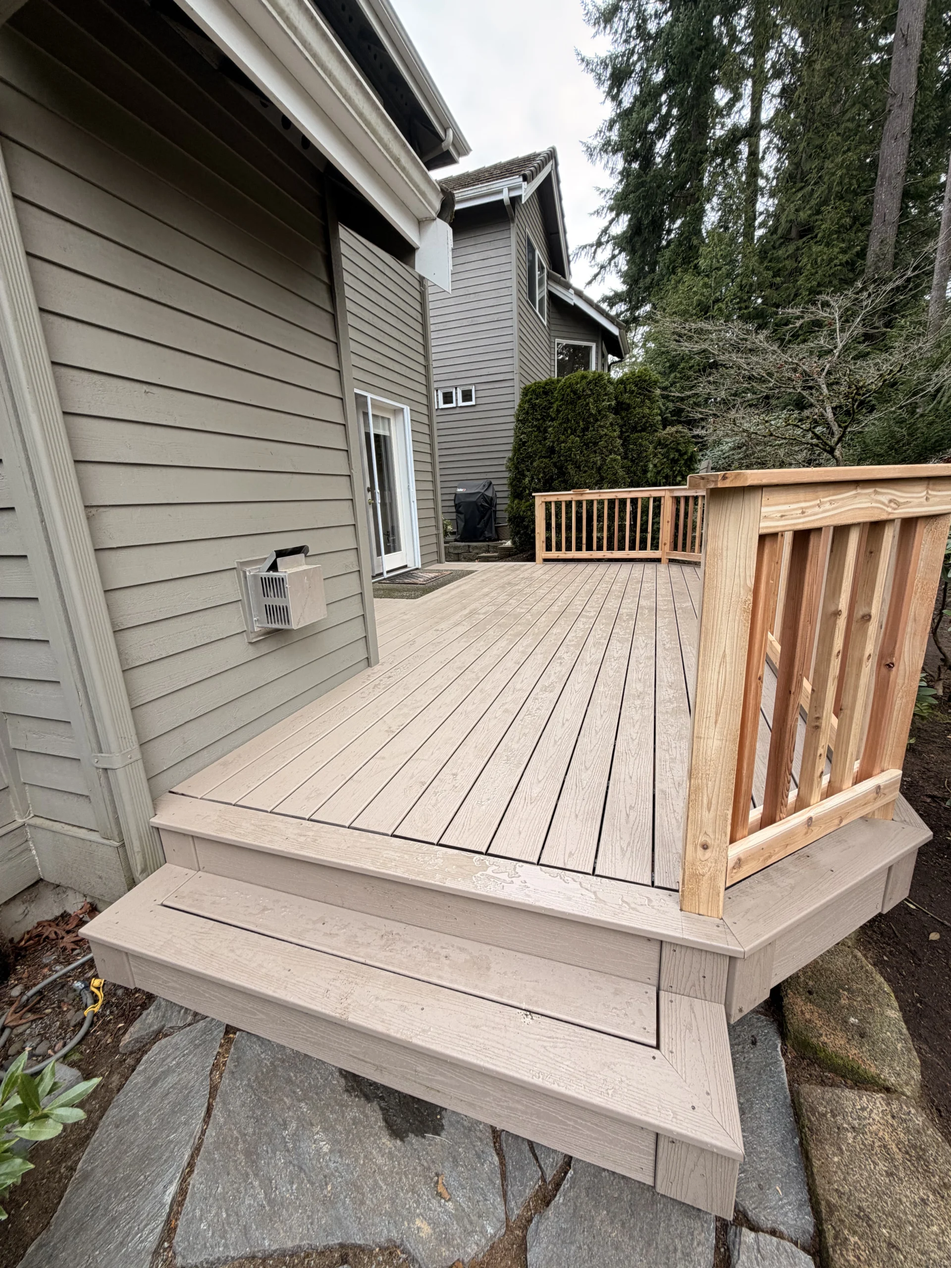 Professional Composite Deck Installation in Mill Creek WA Adjoining a Two-Story Home A durable composite deck installation in Mill Creek WA features wide steps leading up from a stone patio pathway.