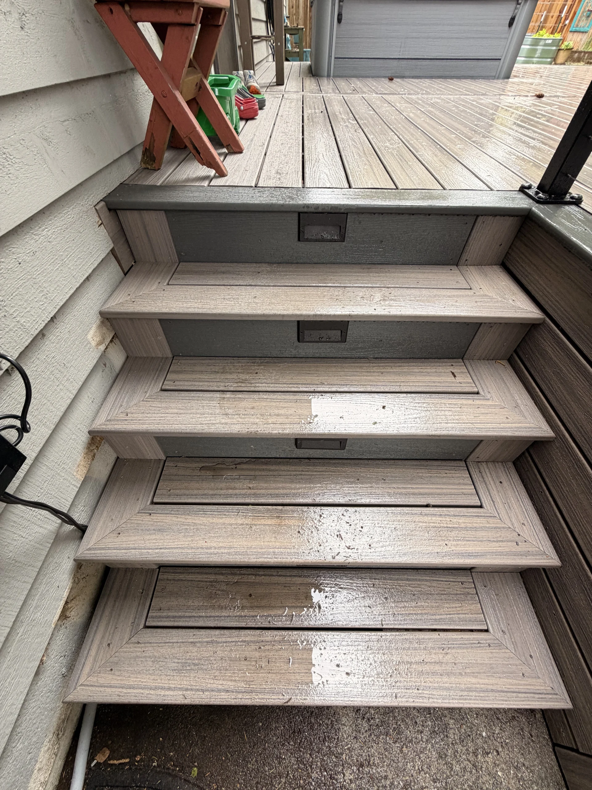 Wet grey stairs with rectangular built-in lights leading to a Composite Deck Installation in Seattle WA.