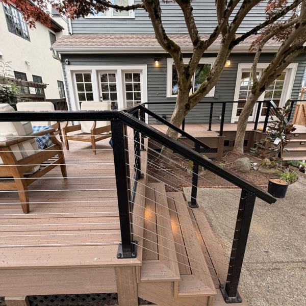 Close Angle Of Black Cable Deck Railings And Composite Steps Under A Tree Canopy.