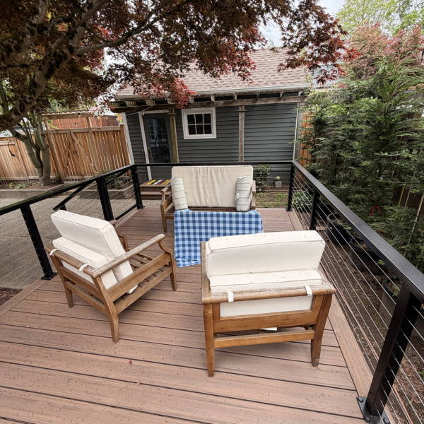 Wooden Patio Armchairs On A Brown Composite Deck With Cable Railings Under A Japanese Maple Tree.
