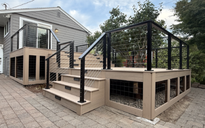 Multi-Level Beige Composite Deck With Black Cable Railings And Under-Deck Wire Mesh Skirting Next To A Paver Patio.