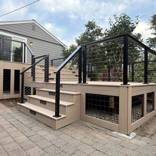 Second-story Trex deck replacement Multi-Level Beige Composite Deck With Black Cable Railings And Under-Deck Wire Mesh Skirting Next To A Paver Patio.