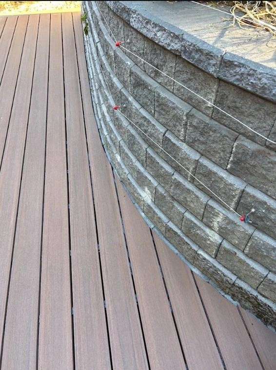 Close-Up Of Composite Deck Boards Curved Seamlessly Against A Stone Retaining Wall Following A Rotted Wood Deck Replacement.