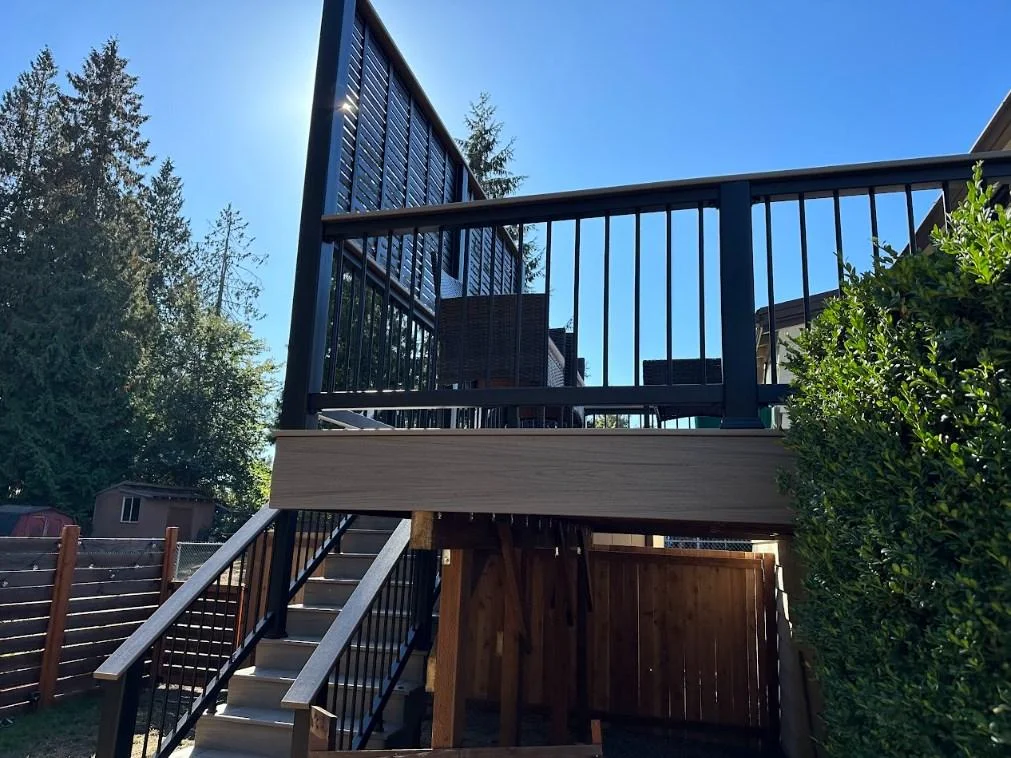 Modern multi-level composite deck with a tall black privacy screen, part of an AZEK Vintage deck replacement in Bellevue. Elevated Composite Deck With Brown Decking And Black Metal Railings And Privacy Screen; Azek Vintage Deck Replacement In Bellevue.