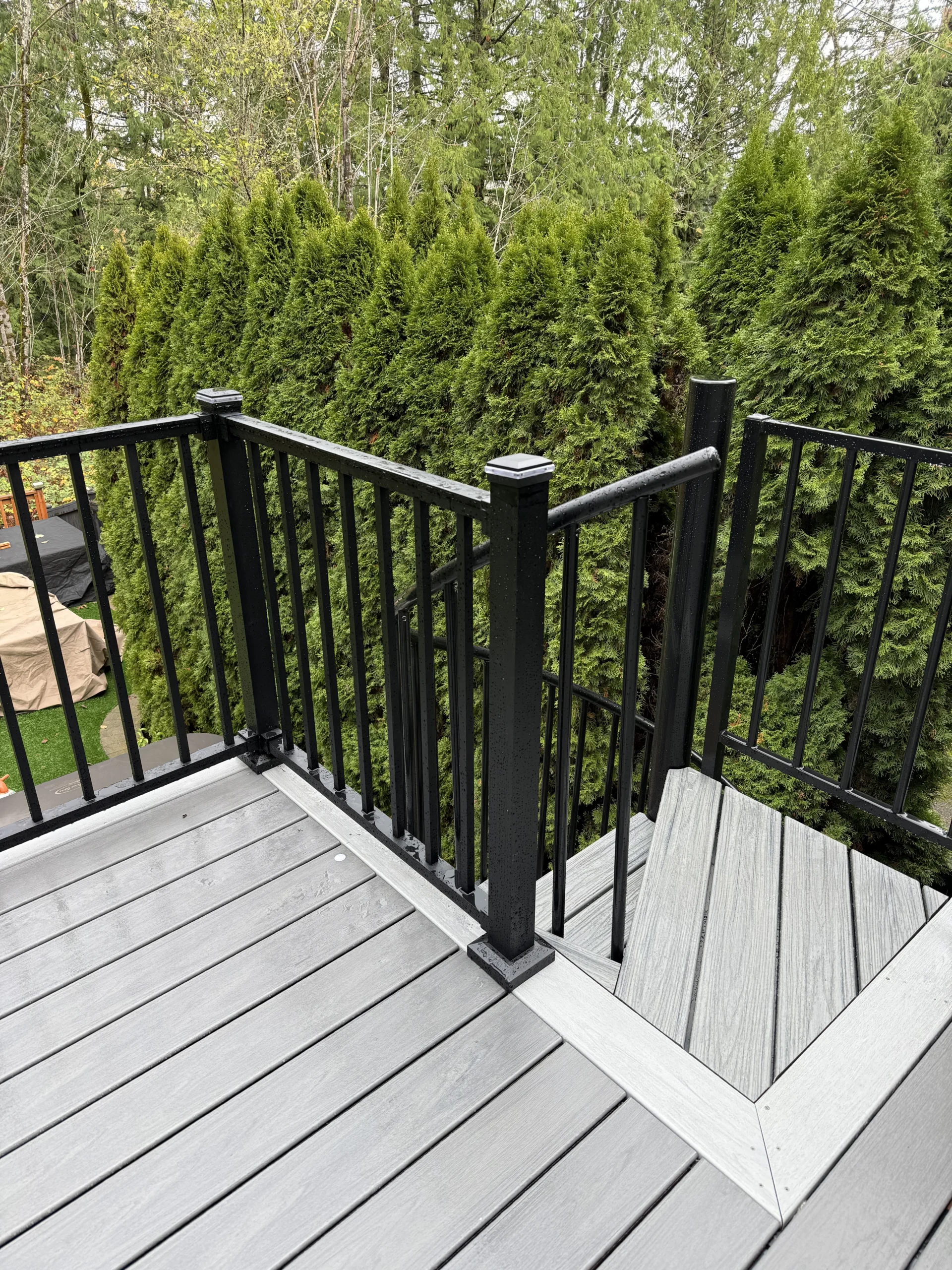Staircase entry view of a newly completed Trex deck replacement in Issaquah surrounded by green trees. Top Landing Of A Spiral Staircase Within A Trex Lineage Composite Deck