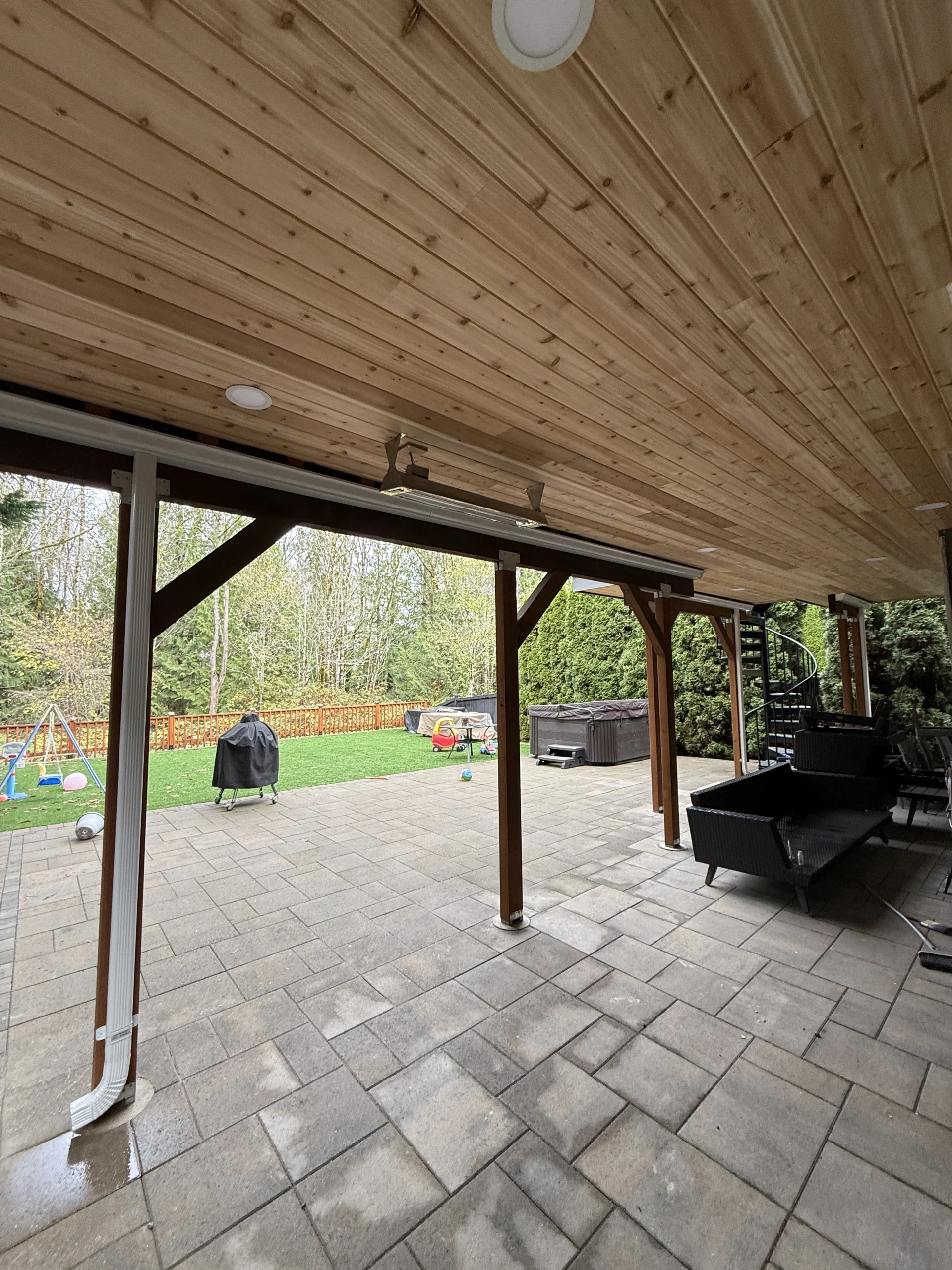 Spacious covered paver patio featuring a custom Trex deck replacement in Issaquah. Covered Paver Patio Beneath An Elevated Deck With A Spiral Staircase