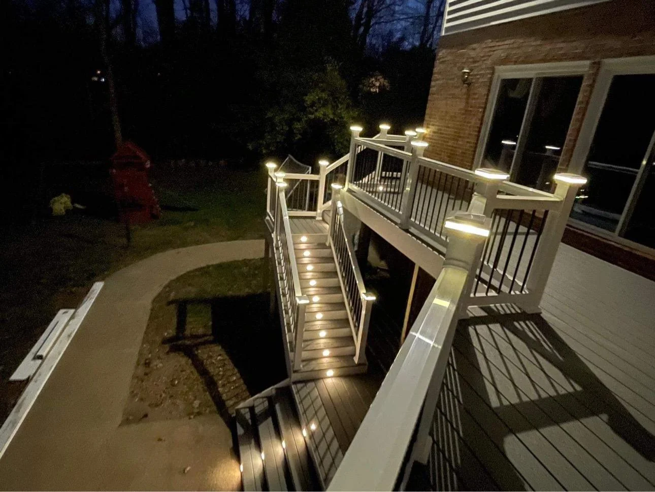 Beautiful deck replacement Everett WA with evening lighting Elevated Deck With Illuminated Stairs And Post Caps Beside A Brick House In Everett, Wa